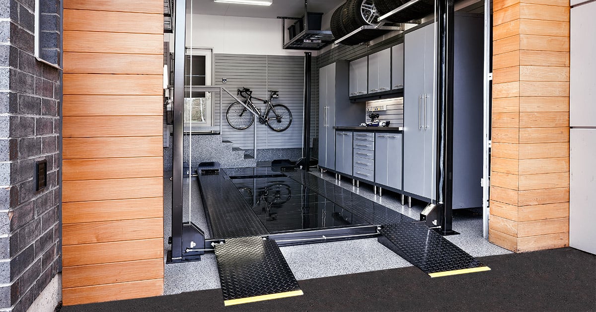Four post car lift with metal ramps in a single car garage.