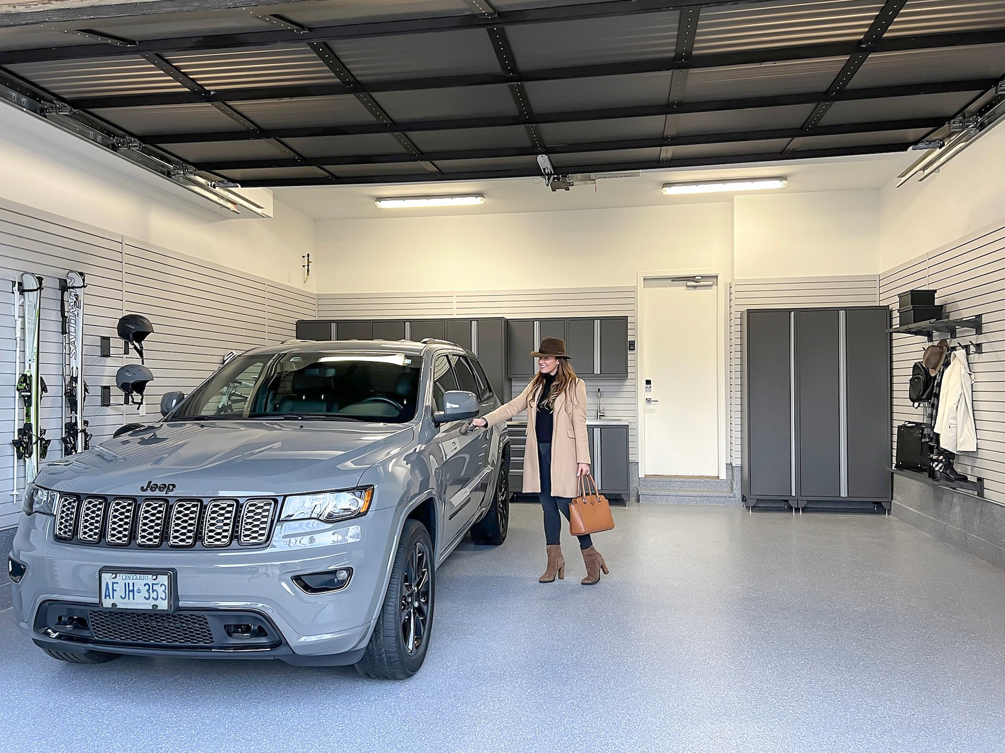 A woman stands beside a parked Jeep in a spacious and luxury garage by Garage Living